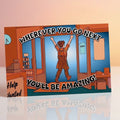 A rectangular illustrated greeting card or print shown standing upright on a reflective surface. The artwork depicts a person with arms raised inside a shop or office, with large text reading “WHEREVER YOU GO NEXT YOU’LL BE AMAZING!” and a “Help Wanted” sign on the left.