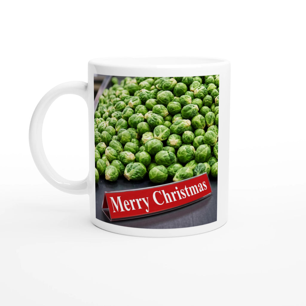 A white ceramic mug featuring a printed graphic of a pile of green Brussels sprouts with a red banner that reads 'Merry Christmas' in white text, set against a plain white background.